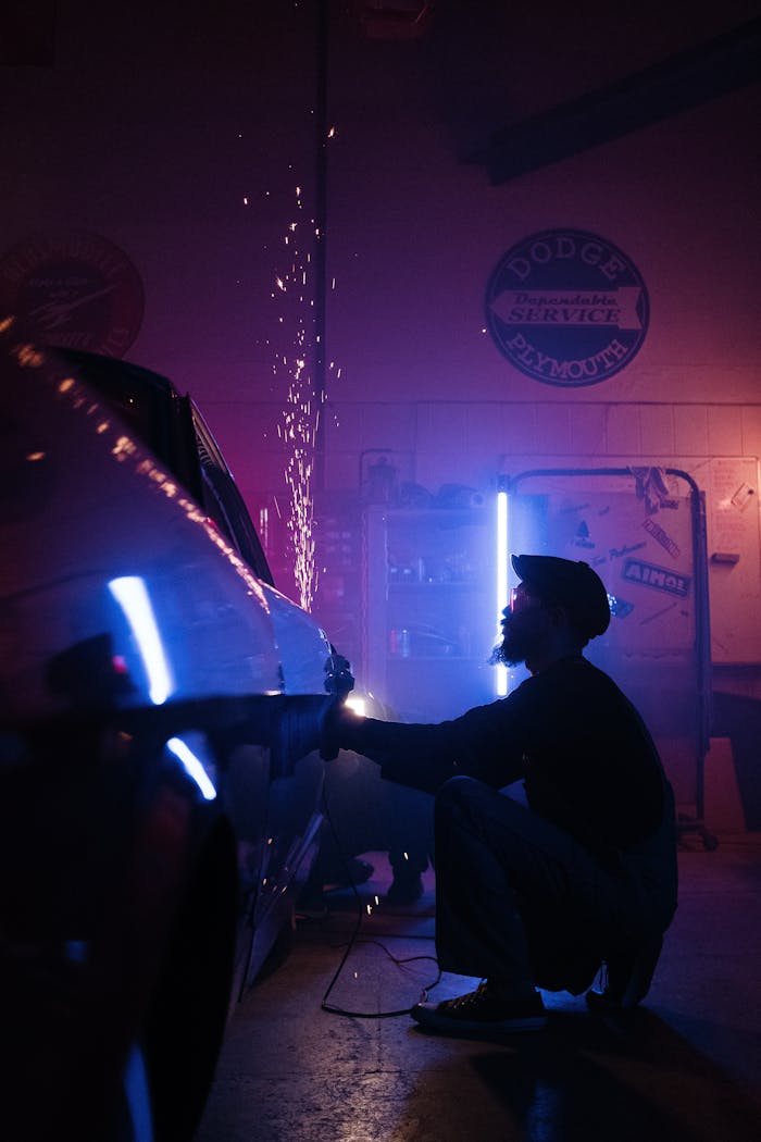 A mechanic is repairing a car in a neon-lit garage, creating sparks from metalwork.